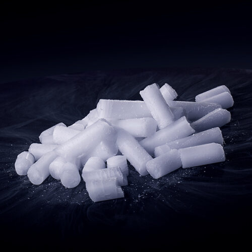 Mehrere zylinderförmige Trockeneis-Nuggets auf dunklem Hintergrund mit feinem Frost.