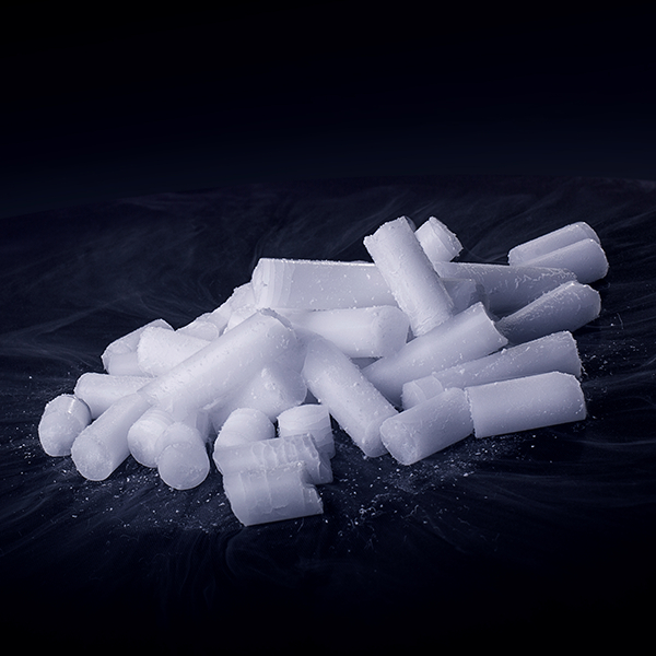 Mehrere zylinderförmige Trockeneis-Nuggets auf dunklem Hintergrund mit feinem Frost.