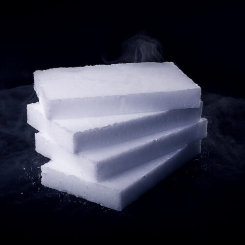 Gestapelte, flache Trockeneis-Scheiben mit Dampfentwicklung auf schwarzem Hintergrund.