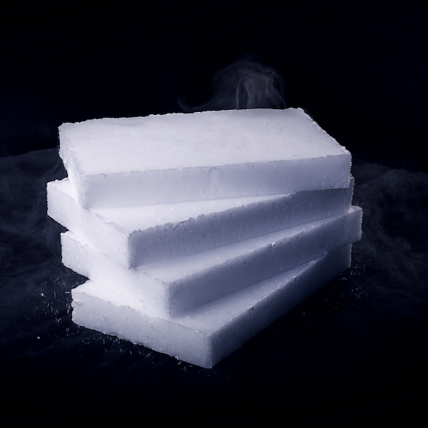 Gestapelte, flache Trockeneis-Scheiben mit Dampfentwicklung auf schwarzem Hintergrund.